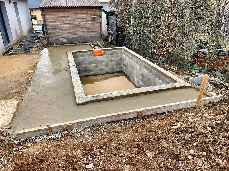 Chantier de construction – Petit bassin en agglo et dalle de plage fraîchement coulée.