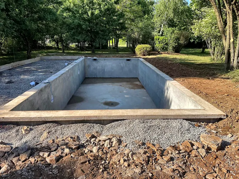 Chantier de construction – Bassin terminé en maçonnerie, dans un jardin arboré.
