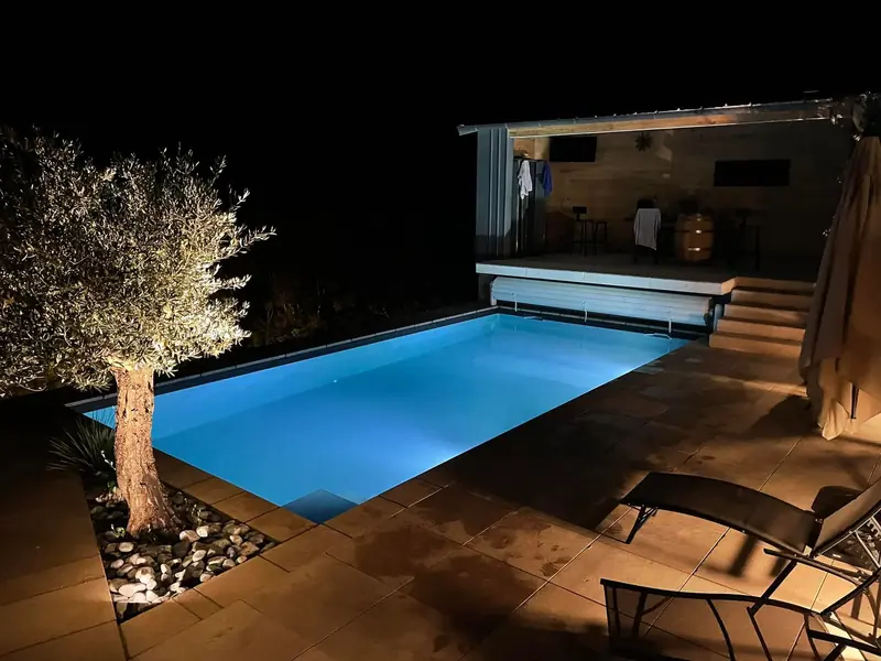 Piscine éclairée la nuit – Éclairage LED subaquatique et terrasse en bois.